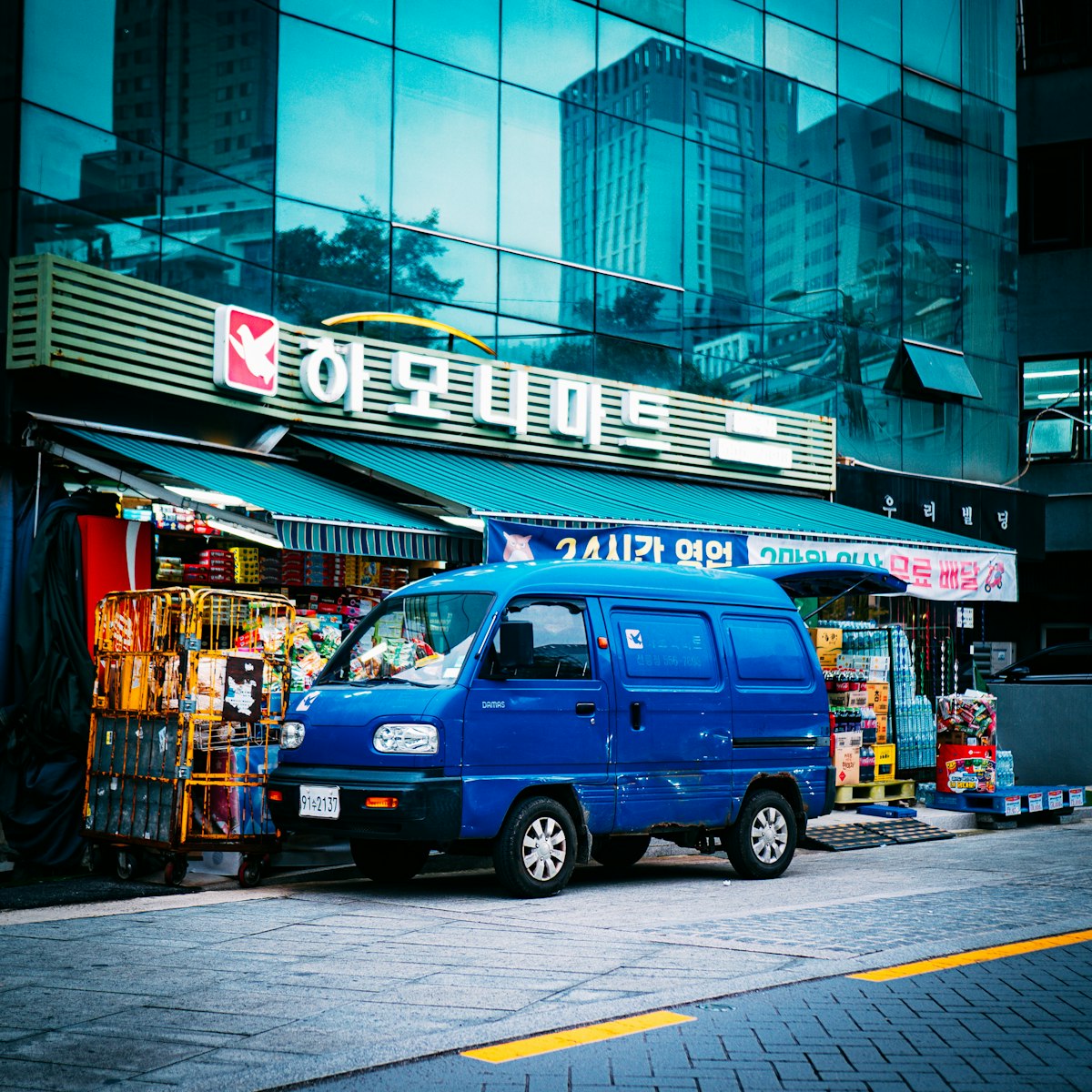 Korean neighbourhood mart advertising 24-hour opening with a delivery van outside
