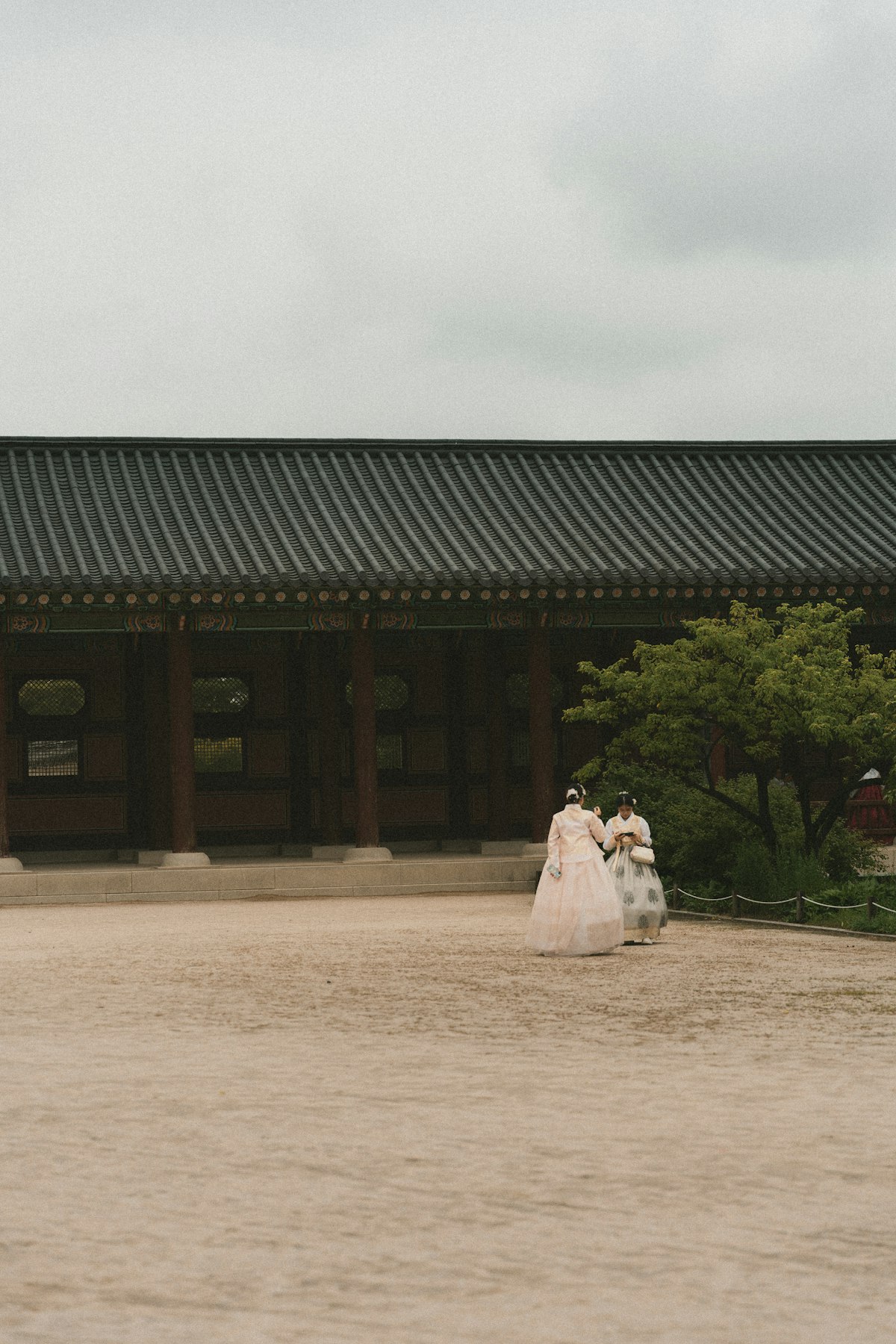 Two visitors in hanbok crossing the courtyard of a Korean palace hall