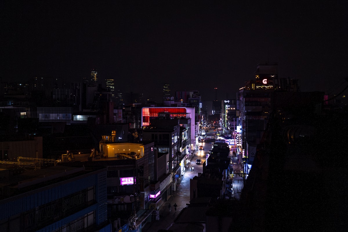 Seoul rooftops at night with a neon-lit street in the distance