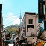 Seoul side street in daylight with N Seoul Tower rising behind the rooftops